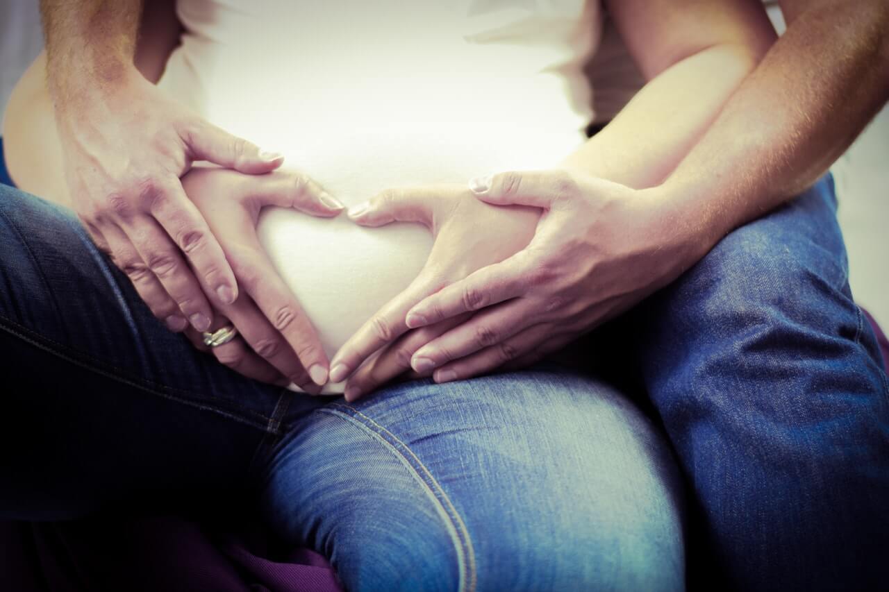 pregnant women with partner's hans touching her around bump