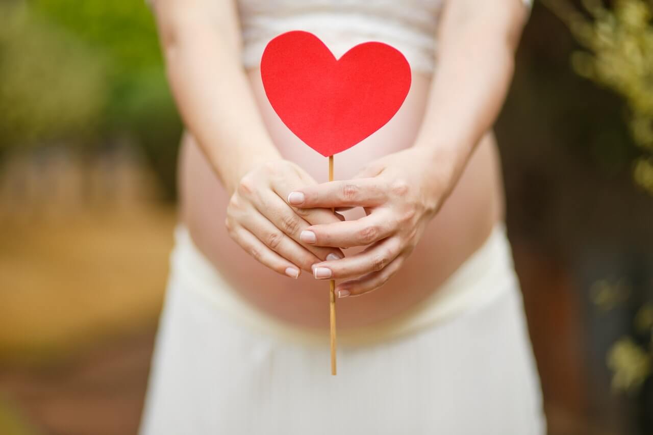 pregnant woman holding heart on stick in from of bump