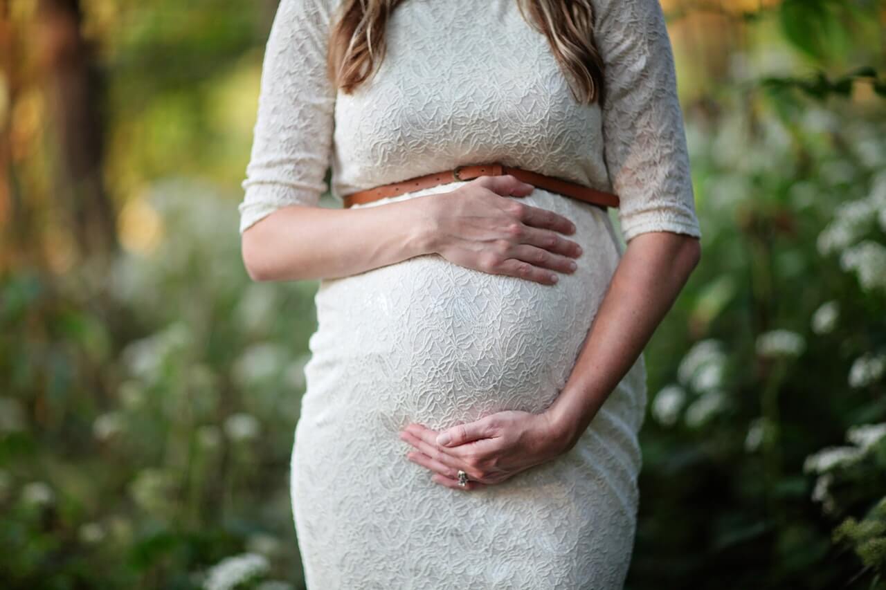 pregnant woman in white dresss holding bump
